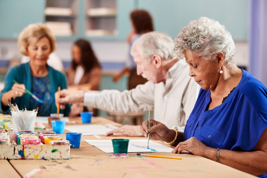 Group Of Retired Seniors Attending Art Class In Community Centre With Teacher Group Of Retired Seniors Attending Art Class