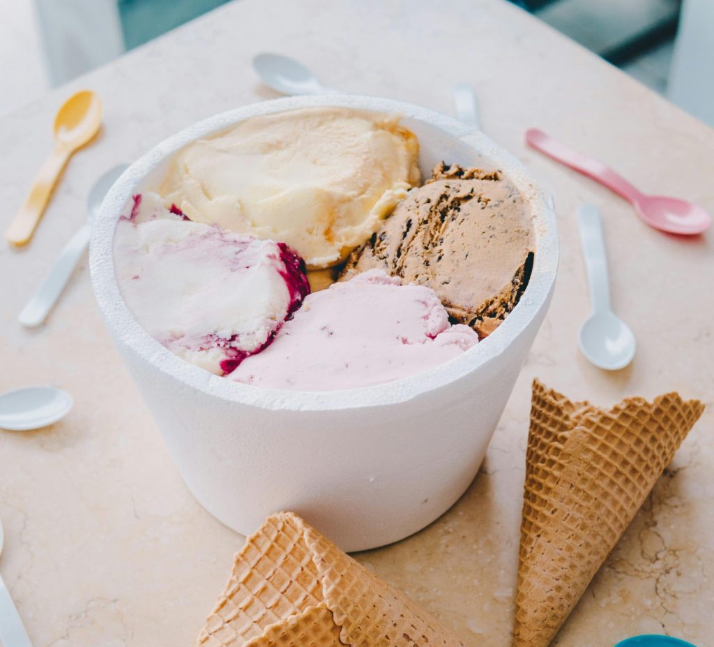 A vibrant display of multi-flavor ice cream with waffle cones and colorful spoons.